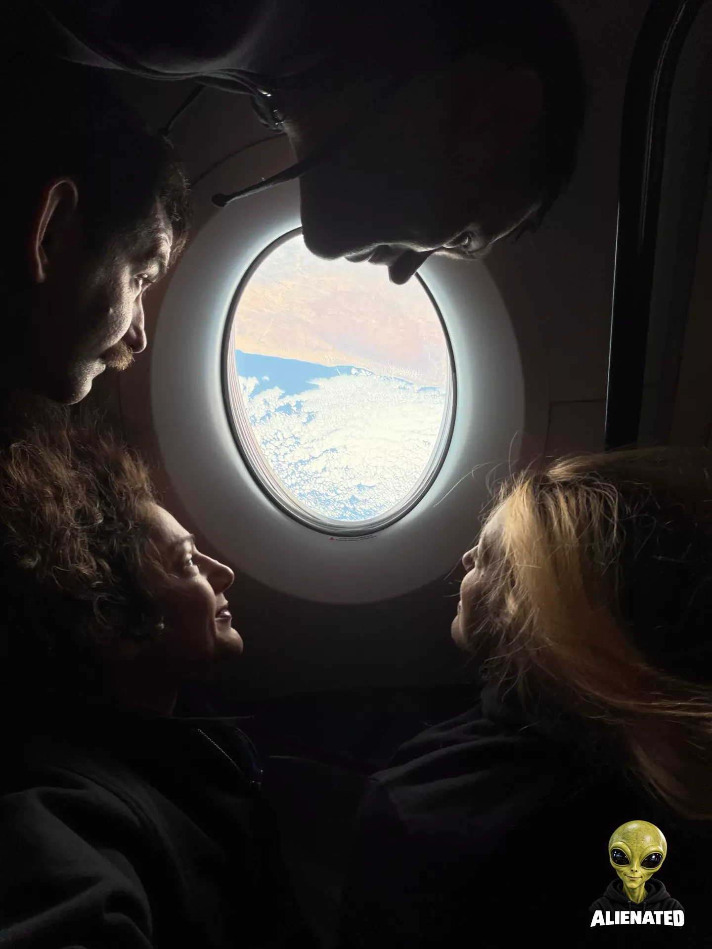 NASA’s SpaceX Crew-12 crew members surround an oval-shaped window aboard a SpaceX Dragon, looking out at clouds above blue water and a tan landmass. From the left, rotating clockwise around the image are NASA astronaut Jack Hathaway, Roscosmos cosmonaut Andrey Fedyaev, ESA (European Space Agency) astronaut Sophie Adenot, and NASA astronaut Jessica Meir. Their faces are illuminated by sunlight streaming through the window.