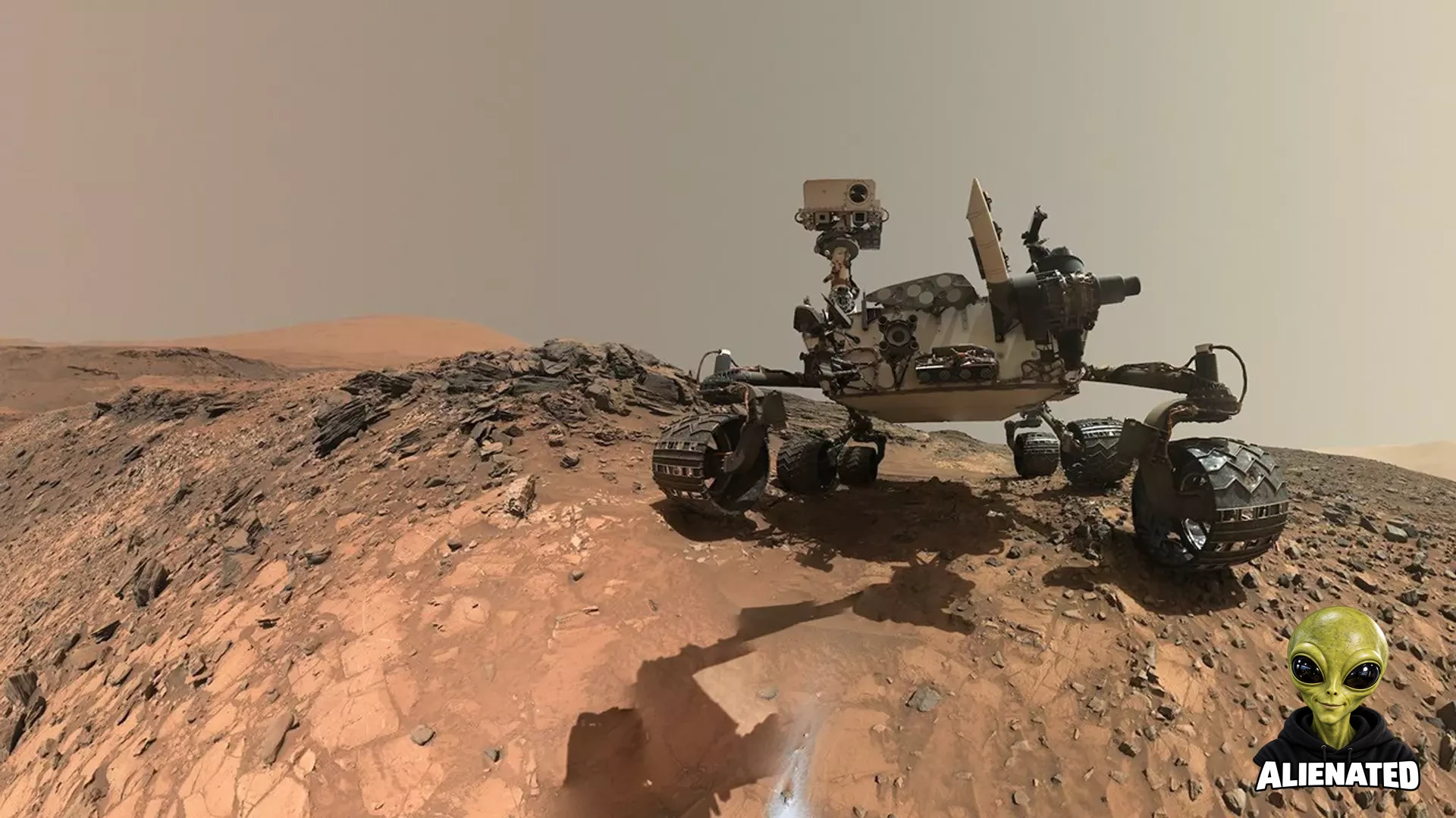 A rover sits on the hilly, orange Martian surface beneath a flat grey sky, surrounded by chunks of rock.