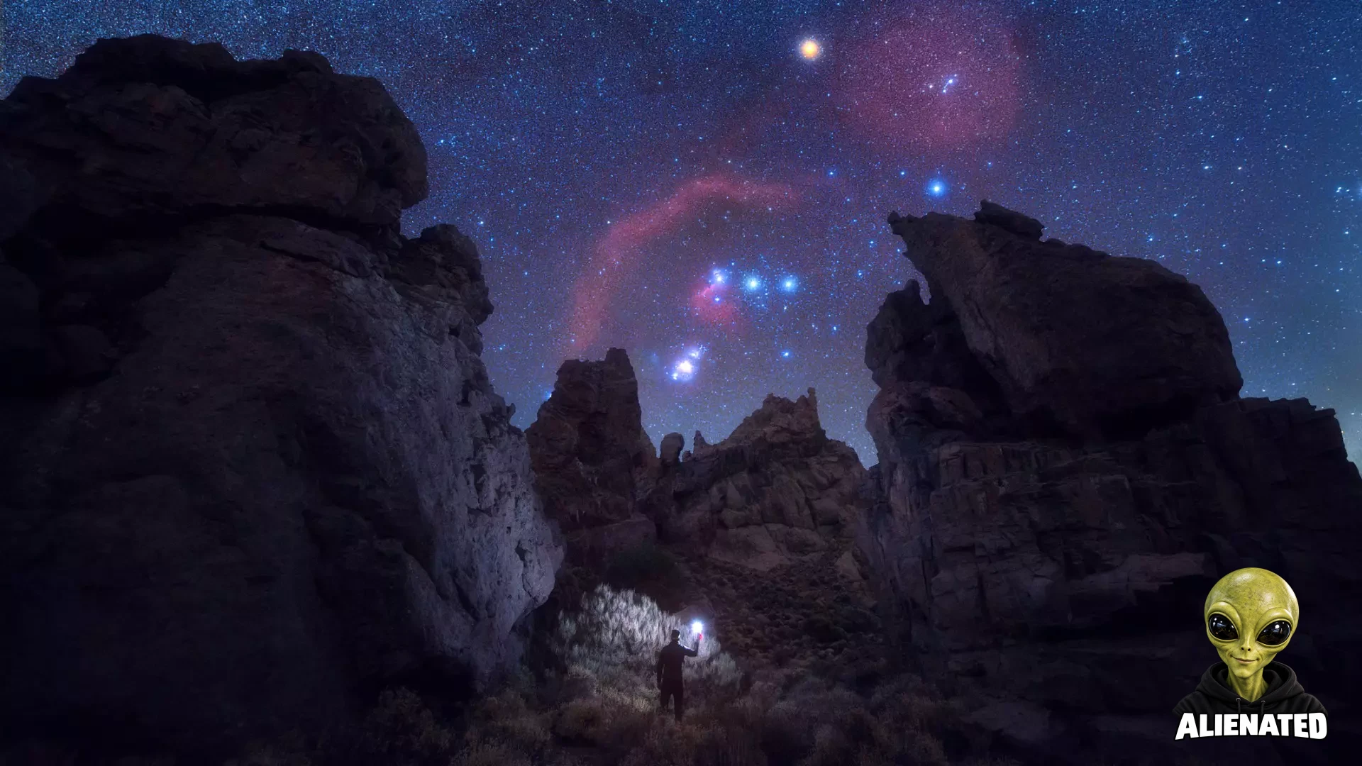 A night sky showing the constellation Orion peaking between large craggy rocks. At the bottom is a human holding up a light.