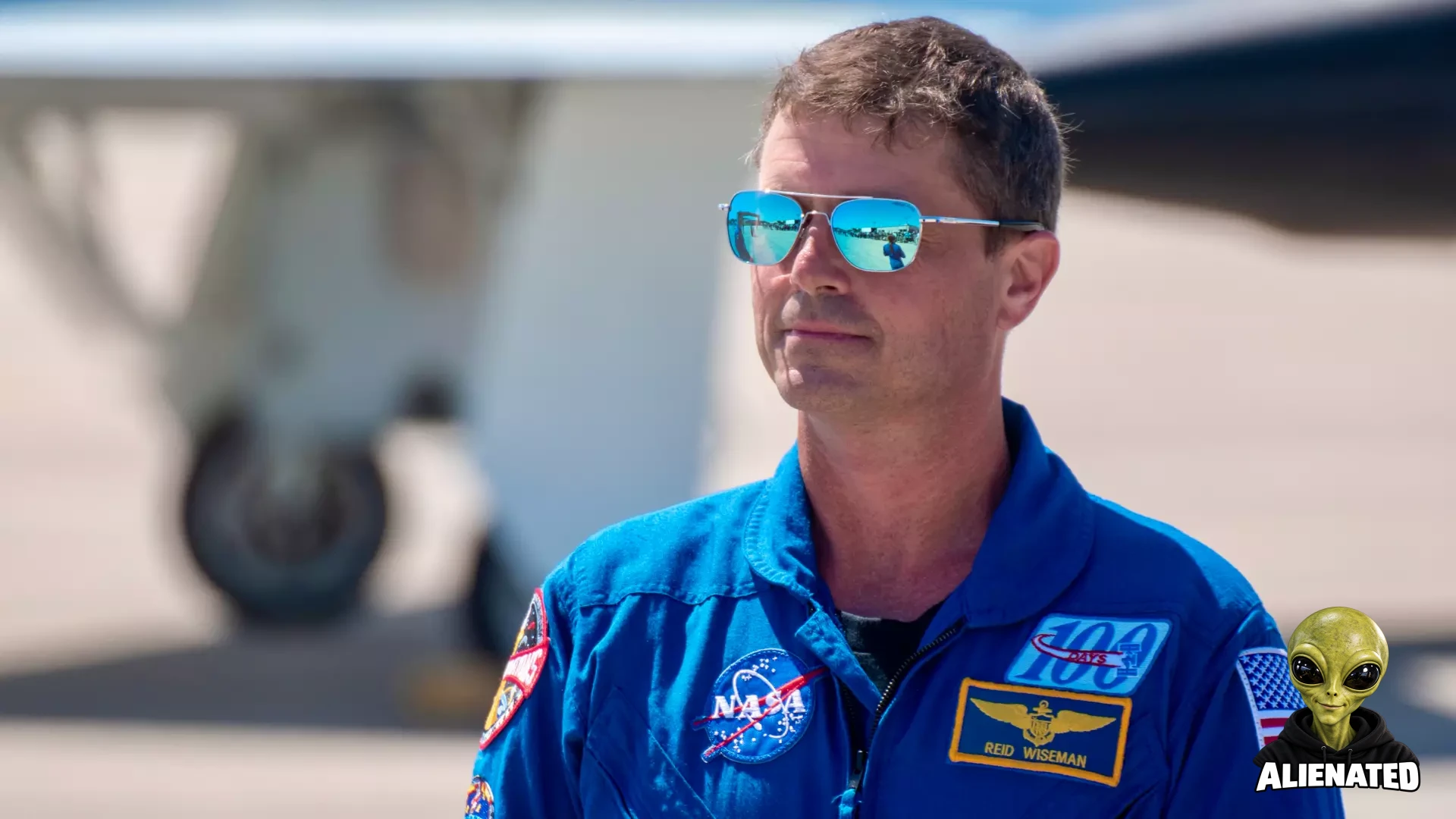 An astronaut in blue jumpsuit stands outside.