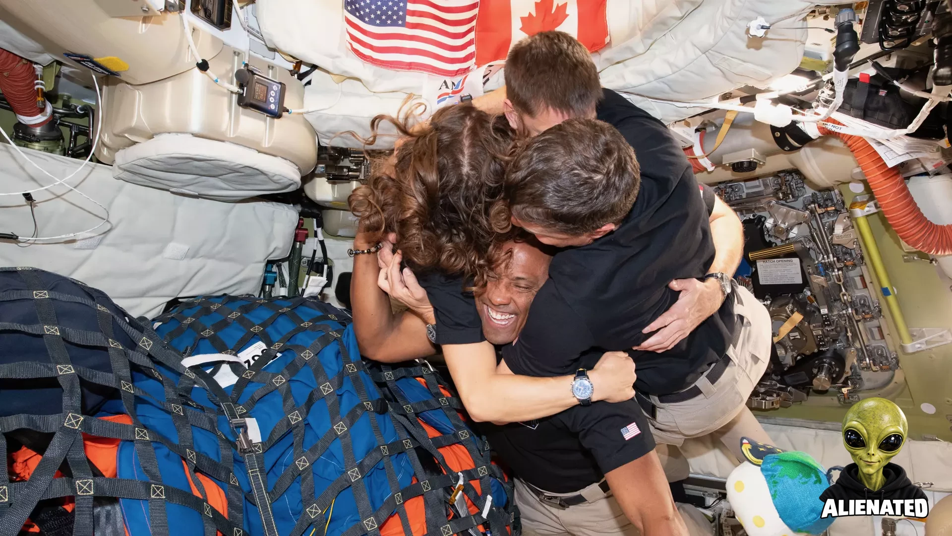 three men and one woman hug inside a space capsule