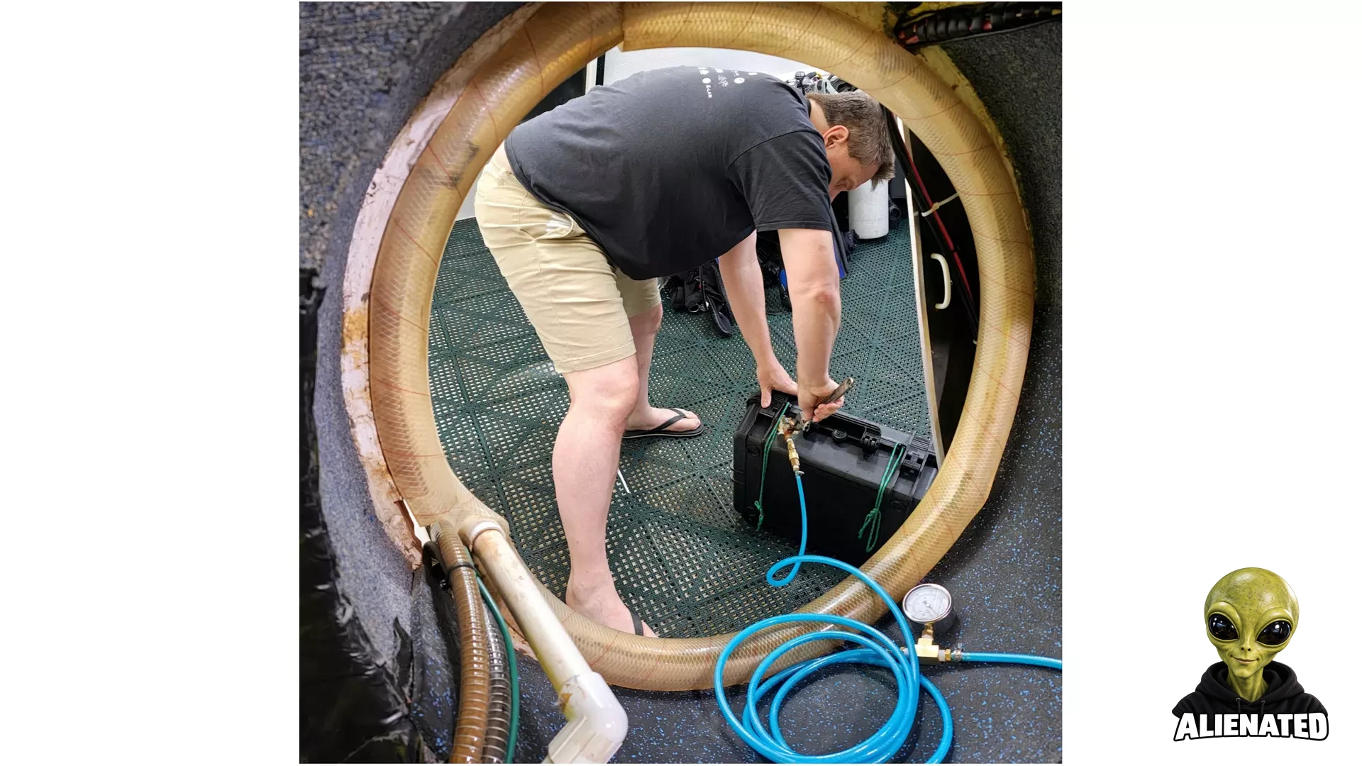a man in shorts and a black t shirt works with a small black suitcase, seen through a circular doorway